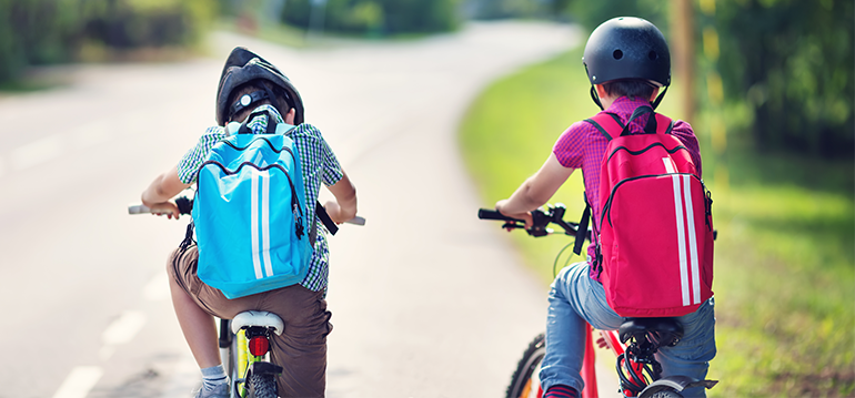 Two kids wearing helmets riding bikes on a road